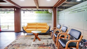 Un área de espera moderna con un sofá amarillo, sillas de madera y una mesa de vidrio.