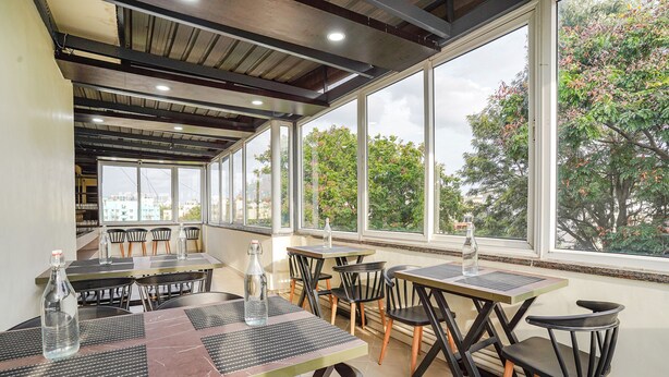 Un comedor interior con mesas y sillas, ventanas amplias y vistas a árboles y edificios.
