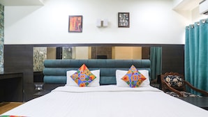 Habitación de hotel con una cama grande, dos almohadones decorativos, una mesita de noche, un espejo y vistas a la ciudad.