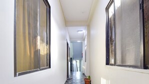 A narrow hallway with large windows on both sides, a tiled floor, and a potted plant near the end. - Fabexpress Nishesh Tower (Ujjain)