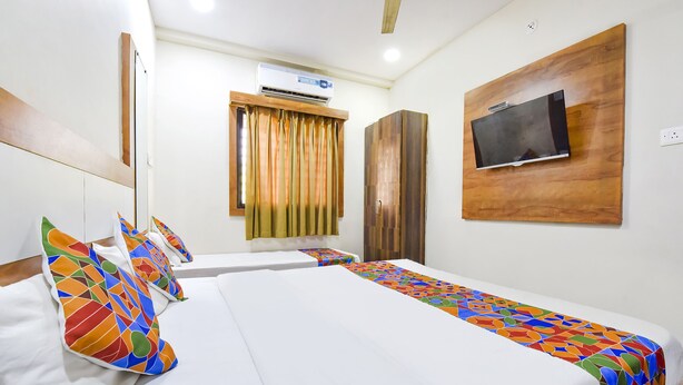 A hotel room with two beds, a TV mounted on the wall, an air conditioning unit, and a window with curtains. - Fabexpress Nishesh Tower (Ujjain)