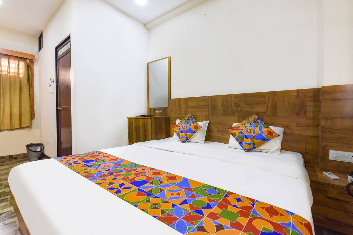 A hotel room with a large bed, a wooden headboard, a mirror, and a colorful bedspread.