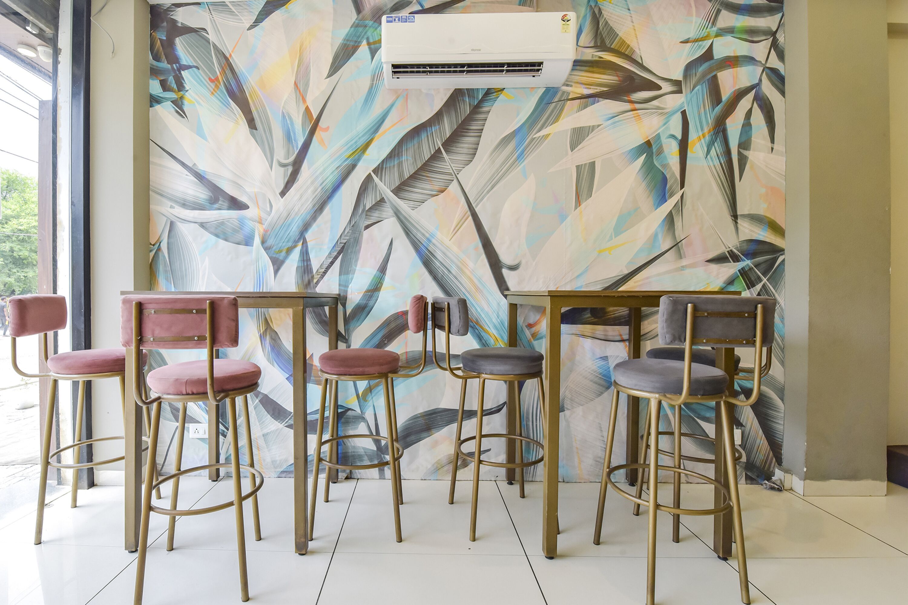 Zona de bar con seis taburetes y una mesa, un equipo de aire acondicionado grande y una pared con un mural de motivos vegetales.