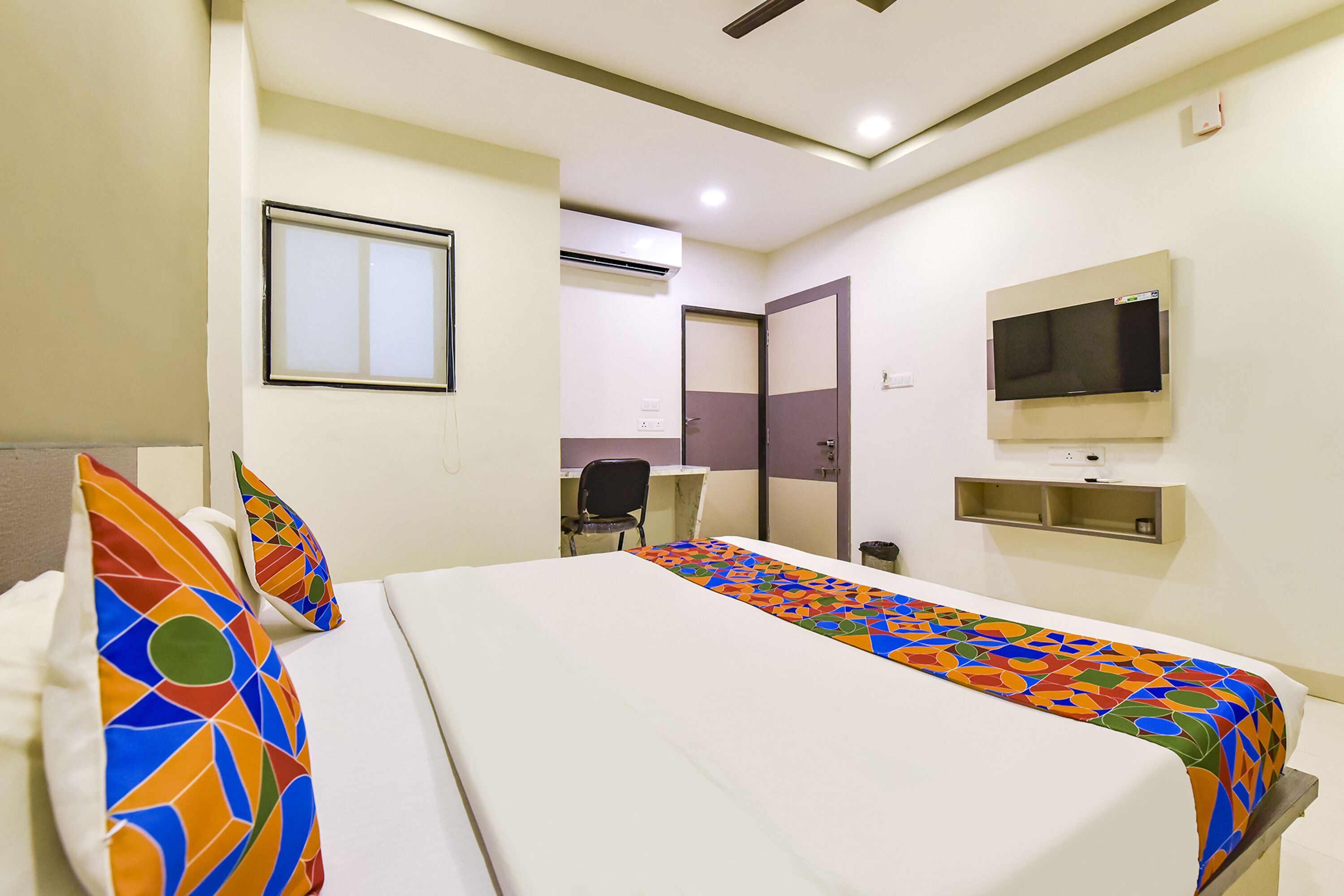 A hotel room with a bed, pillows, a TV, and a desk.