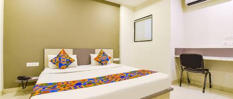 A hotel room with a bed, a desk, and an air conditioning unit.