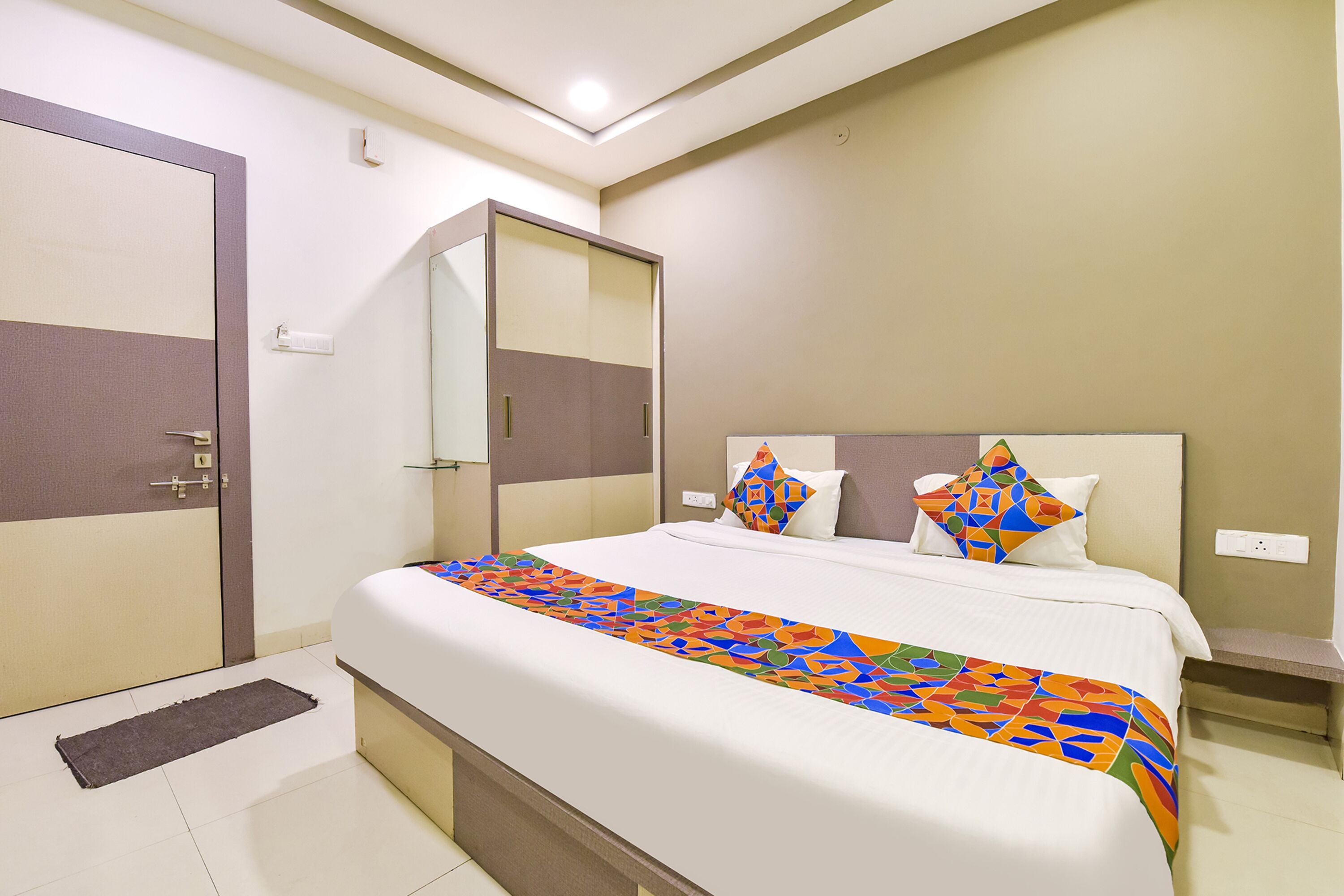 A hotel room with a large bed, a bedside table, a nightstand, a mirror, and a door.