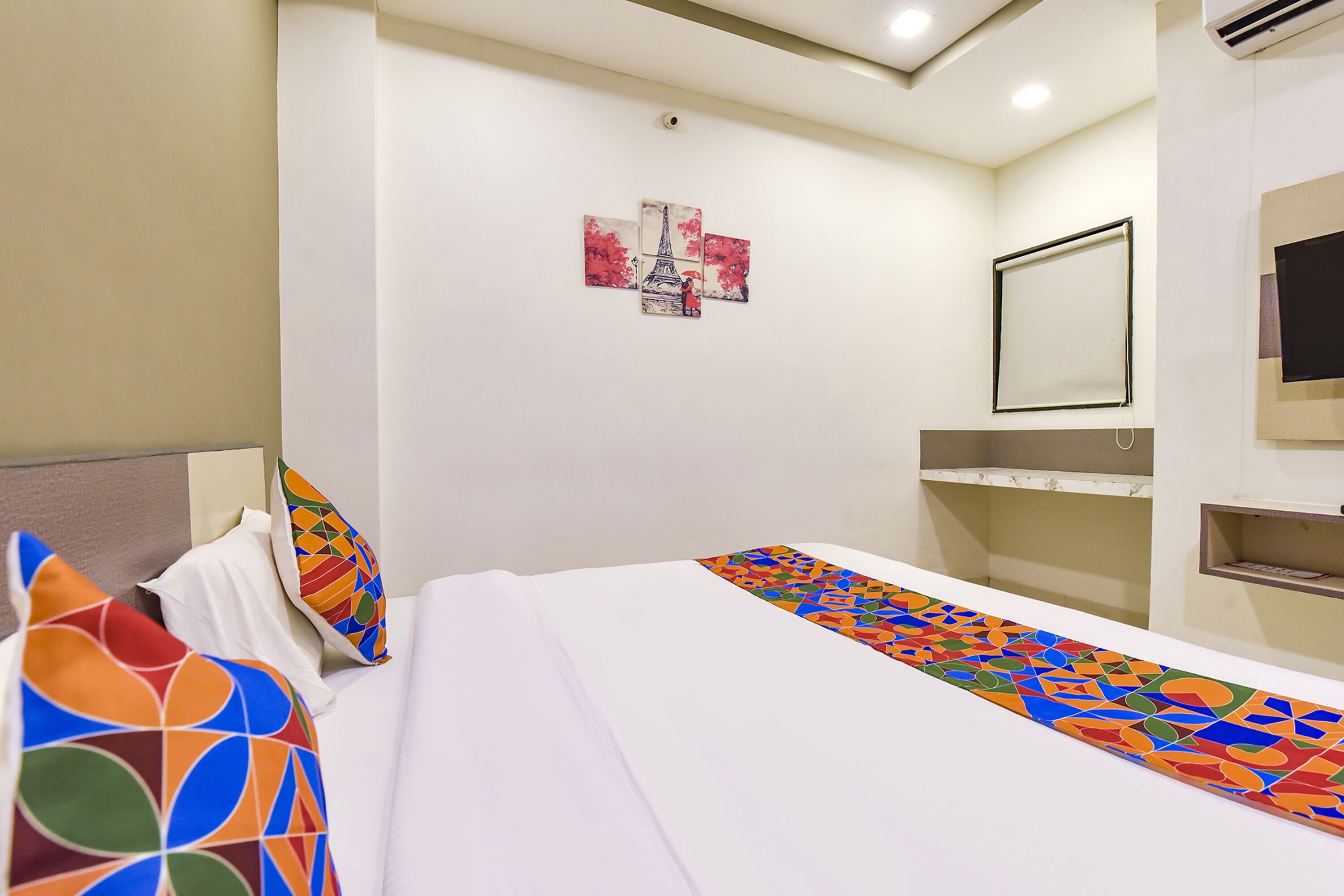 Una habitación de hotel con una cama, un cabecero colorido, un espejo fijado a la pared y una pequeña estantería.