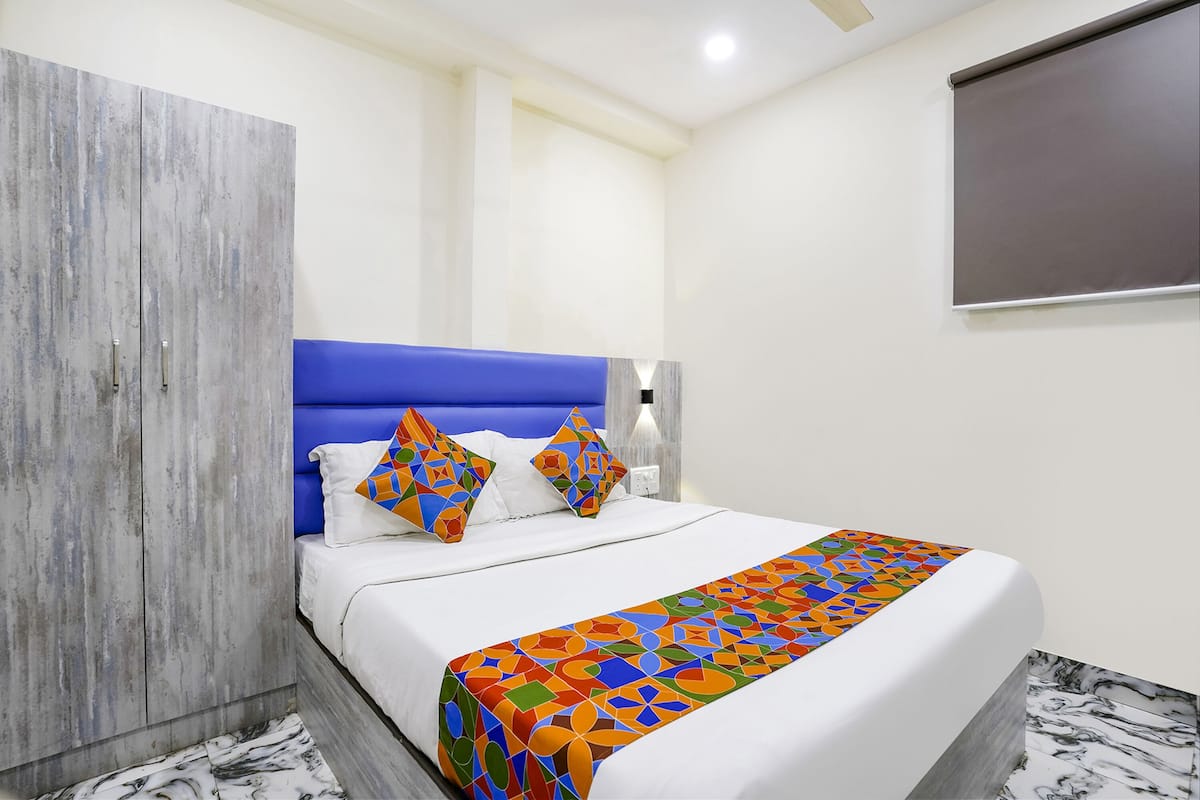 A bedroom with a bed, blue headboard, white bedding, colorful throw, and a wooden wardrobe.
