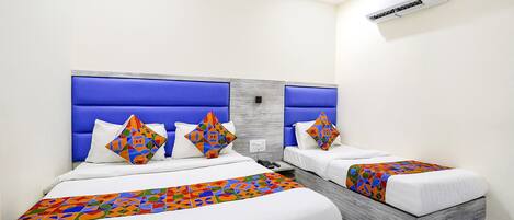 Ein Hotelzimmer mit zwei Betten, jeweils mit blauem Kopfteil, weißer Bettwäsche und farbenfrohen, geometrisch gemusterten Bettdecken.