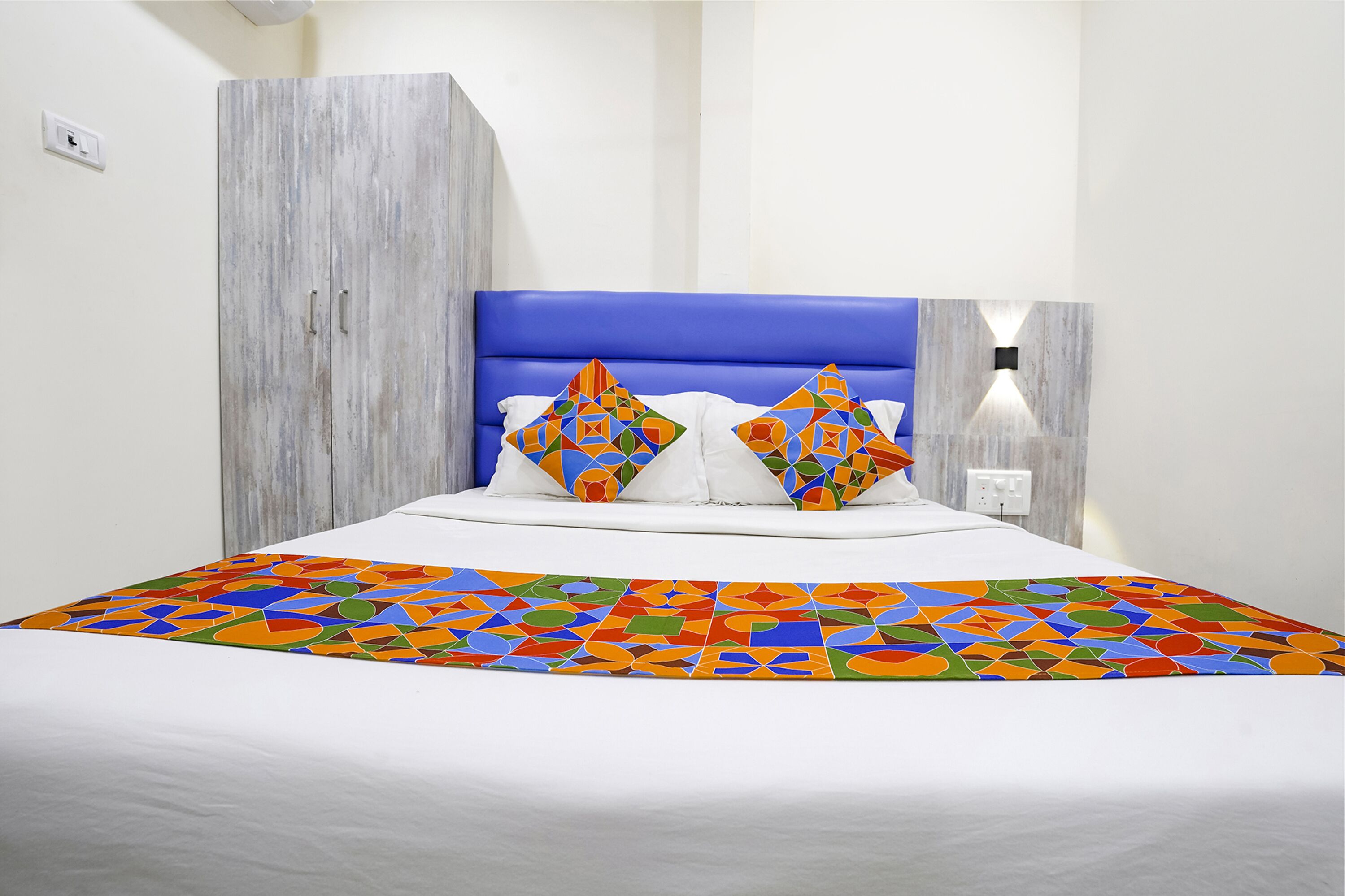 A bed with a blue headboard, white bedding, and colorful geometric pillows.