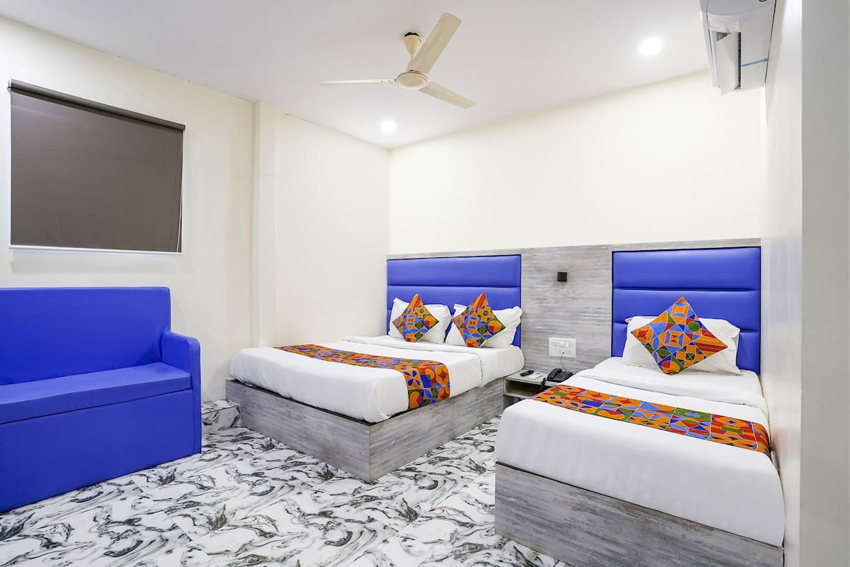A hotel room with two beds, a blue sofa, a ceiling fan, and a marble-patterned floor.