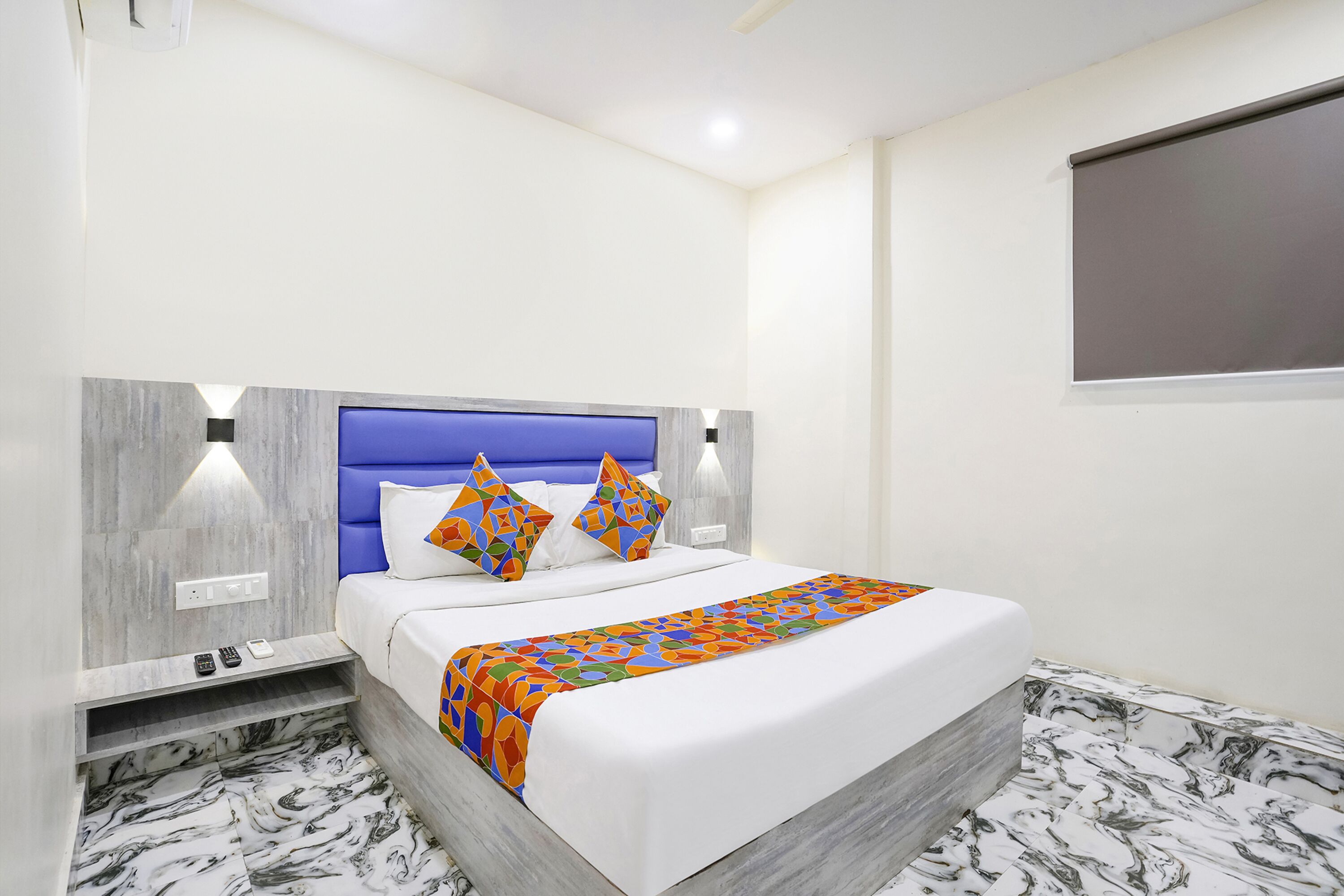 A modern hotel room with a bed, a nightstand, a wall-mounted TV, and a marble-patterned floor.