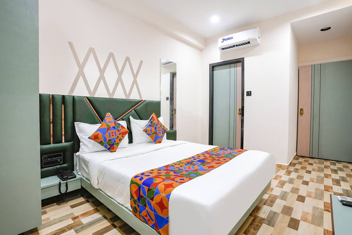 A hotel room with a bed, a bedside table with a phone, an air conditioner, and a check-in counter.