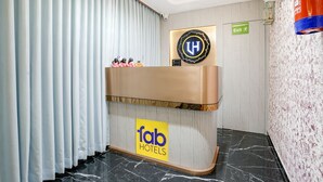Un espace d’accueil d’hôtel comprenant un comptoir de réception, un panneau indiquant la sortie de secours et un logo sur le mur.