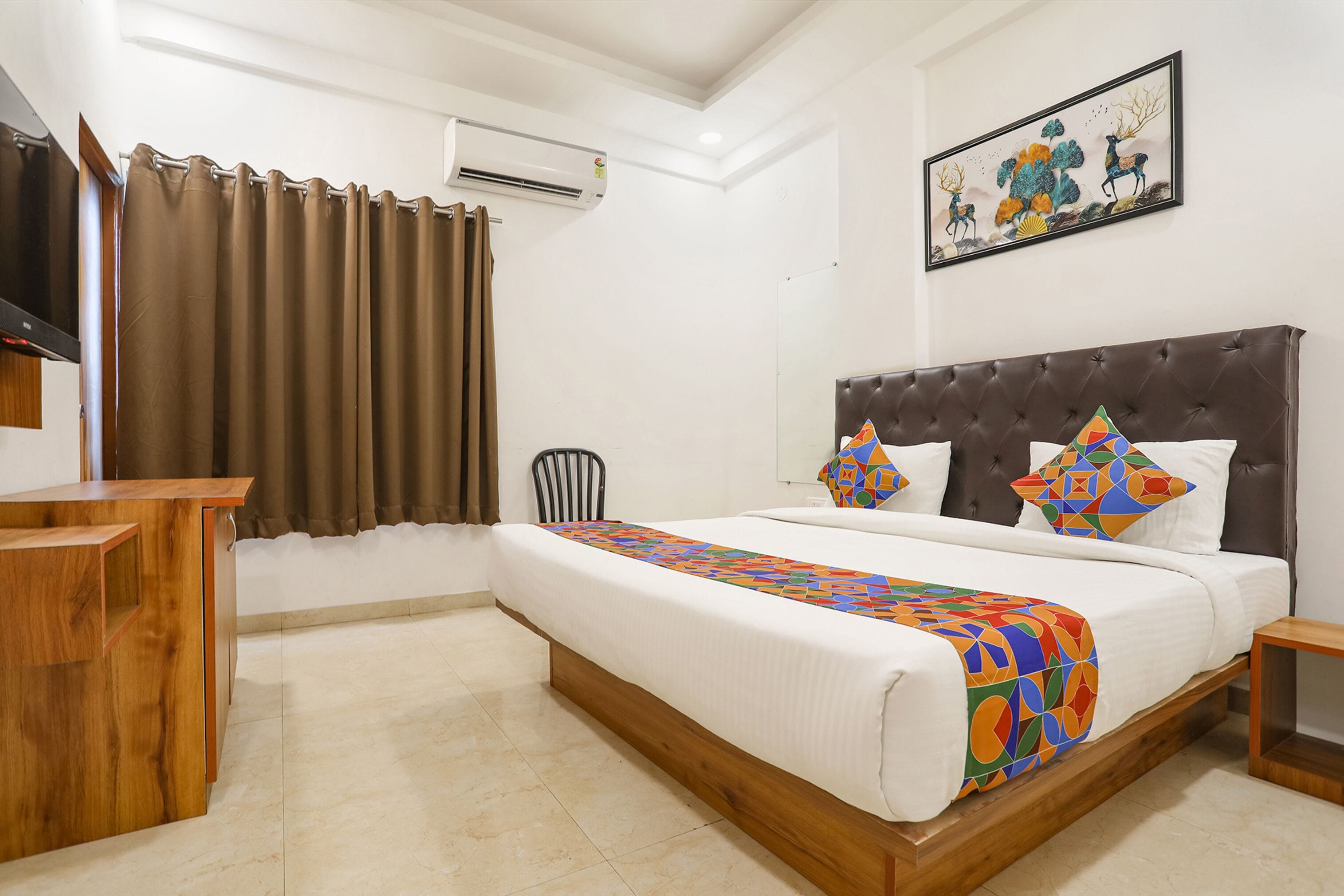 A hotel room with a bed, a wooden desk, a chair, a TV, and an air conditioner.