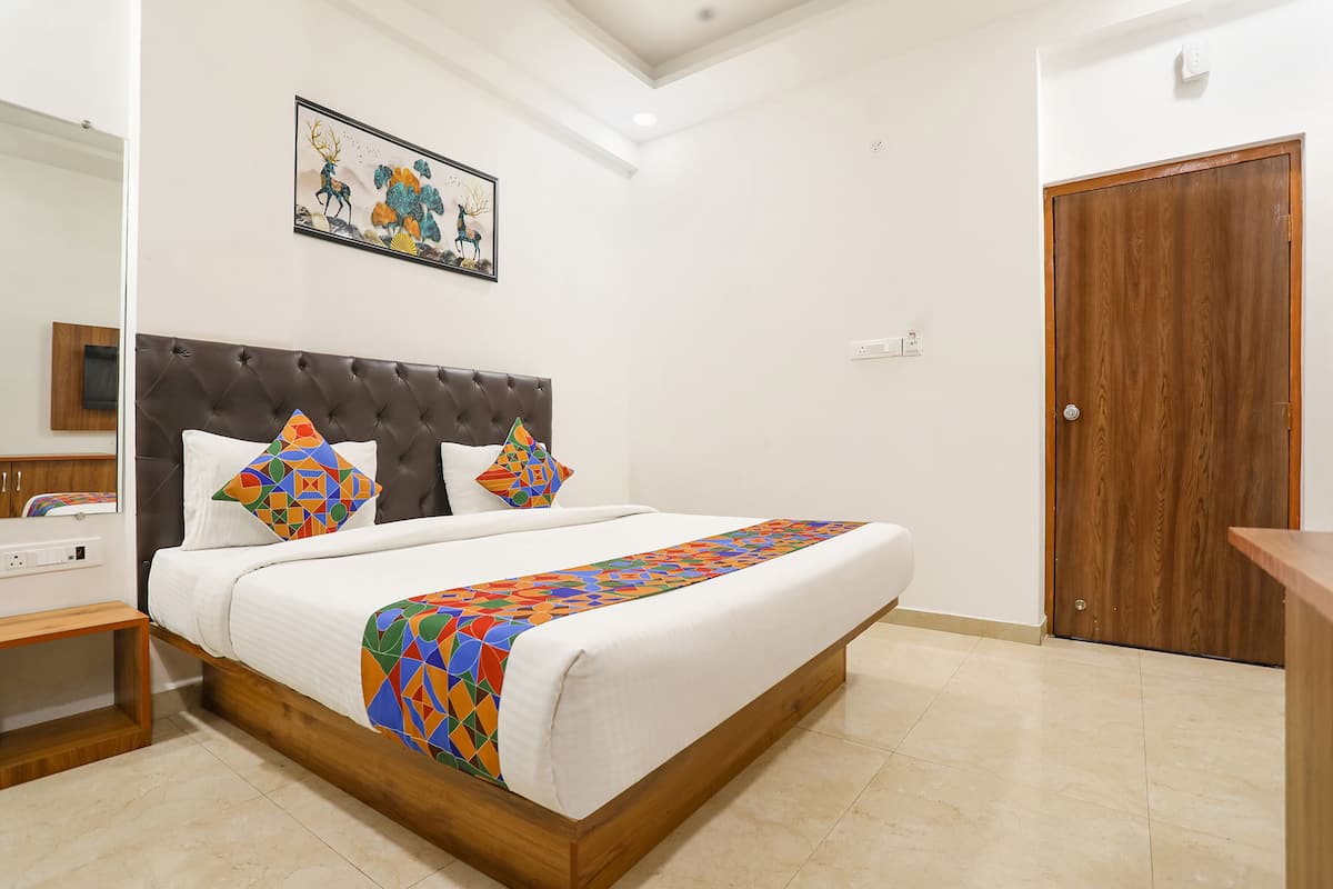 A neatly made bed with a patterned bedspread and two decorative pillows, a wooden headboard, a wooden door, and a framed artwork on the wall.