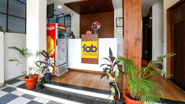 Zona de recepción de hotel con un mostrador de madera, un letrero que dice 'fab hotels' y plantas en macetas.