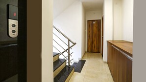 Un pasillo con una puerta de madera, una escalera con barandilla y un panel de ascensor negro.