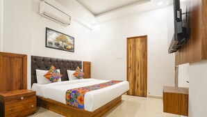Un dormitorio con cama, cabecera de madera, una mesita de noche, televisor montado en la pared y una puerta.