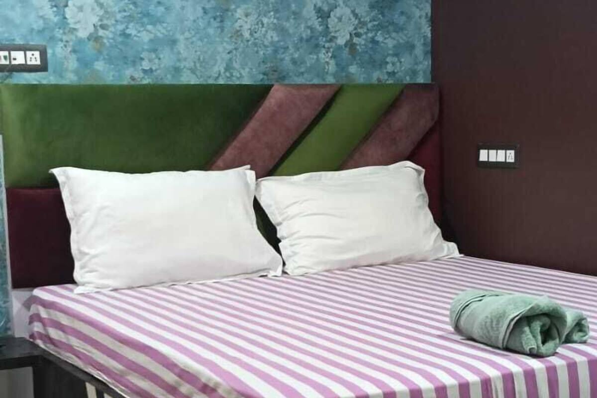 Un lit avec une couvre-lit à rayures, une tête de lit recouverte d’un tissu vert et des oreillers blancs.