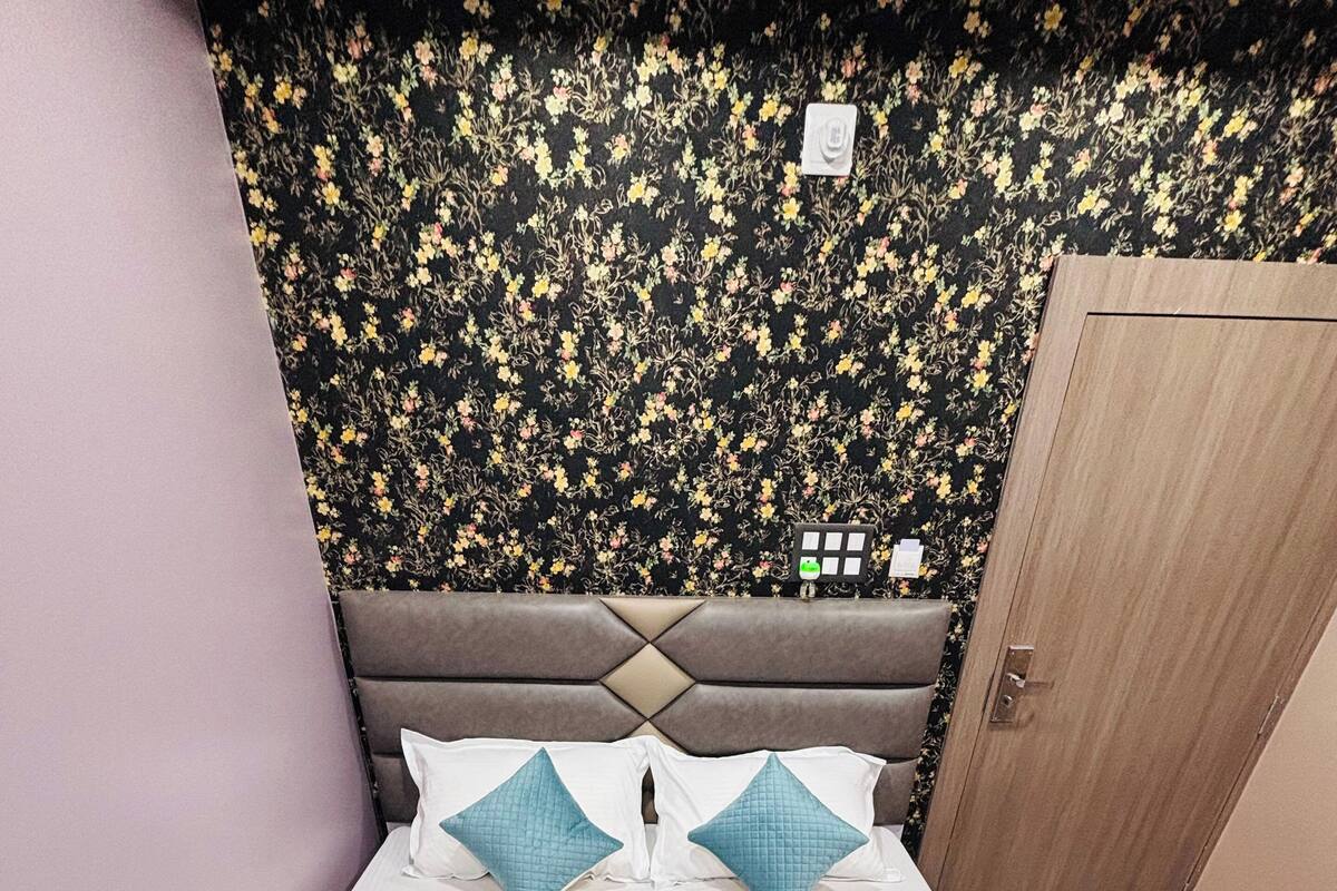 Un lit recouvert d’une courtepointe turquoise matelassée, avec deux oreillers et une tête de lit, le tout placé devant un mur recouvert d’un papier peint à motifs floraux.