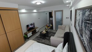 A modern bedroom with a bed, a TV, a sofa, and a large window with a cityscape view. - Gatundu Heights Apartments Kileleshwa (Nairobi)