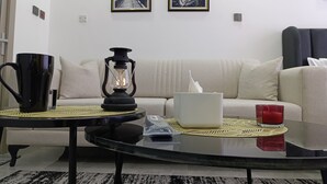 A living room with a sofa, a coffee table, a black mug, a lantern, and two framed pictures on the wall. - Gatundu Heights Apartments Kileleshwa (Nairobi)