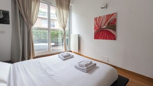 A hotel room with a bed, a window with curtains, a radiator, and a painting on the wall. - Italianway Comfort - Savona 123 (Milan)