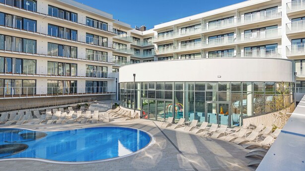 Un hotel moderno con piscina, lettini prendisole e una zona relax in vetro.
