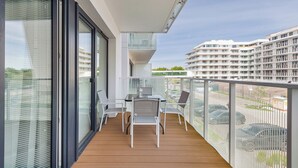 Un balcone con pavimento in legno, sedie bianche e un tavolo.