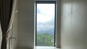 Un baño con bañera, ducha y ventana con vistas a un paisaje verde.
