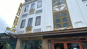 Un edificio con un letrero dorado grande, un ventanal decorativo destacado y un coche rojo estacionado al frente.