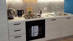 A modern kitchen with white cabinets, a built-in oven, a sink, and a countertop with various appliances. - Turiddu Apartment- Casa Vacanze Giardini Naxos (Taormina)