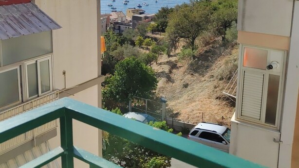A balcony with a view of the sea, a parked car, and a building with a tiled roof. - Turiddu Apartment- Casa Vacanze Giardini Naxos (Taormina)