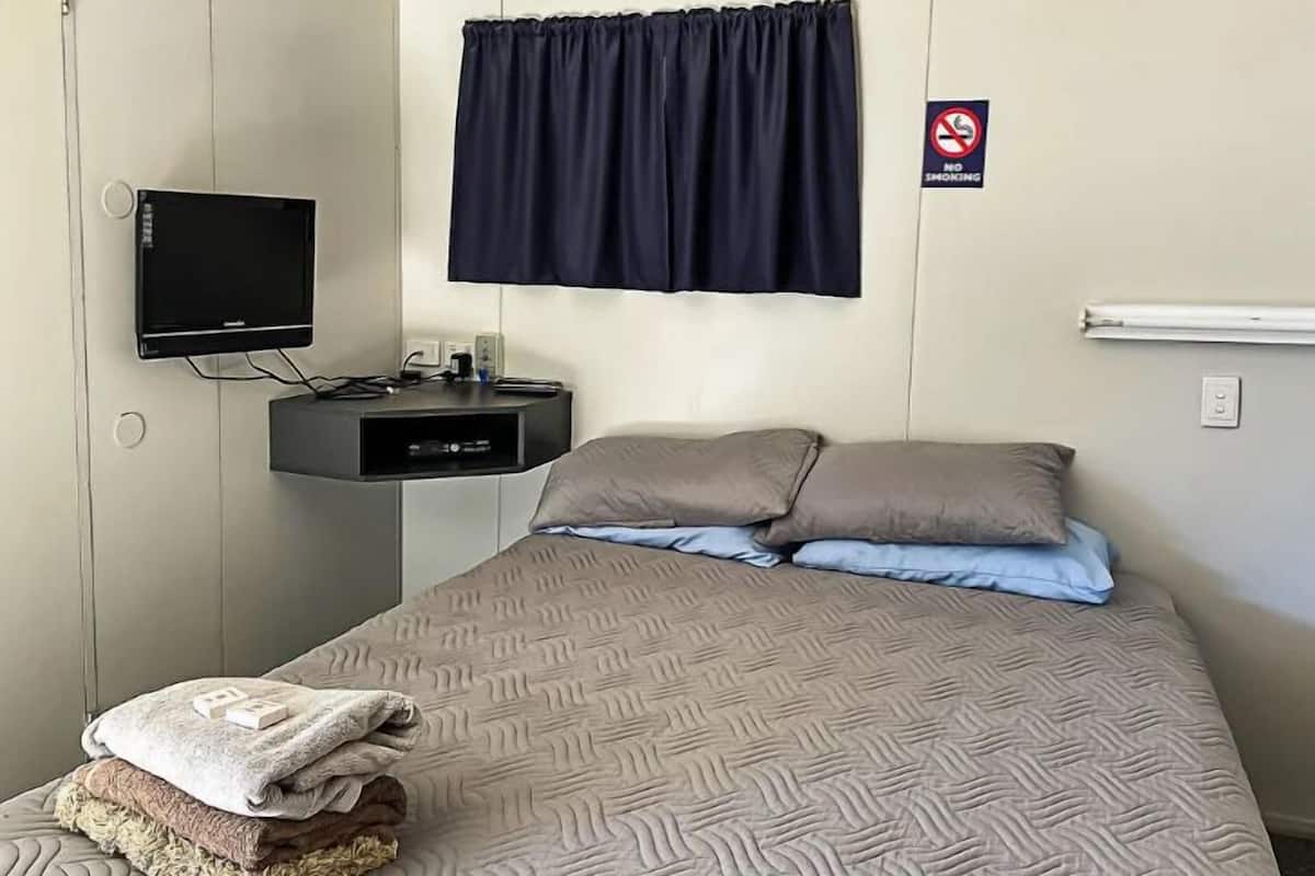 Habitación de hotel con cama, televisión, un pequeño escritorio y un cartel de prohibición de fumar.
