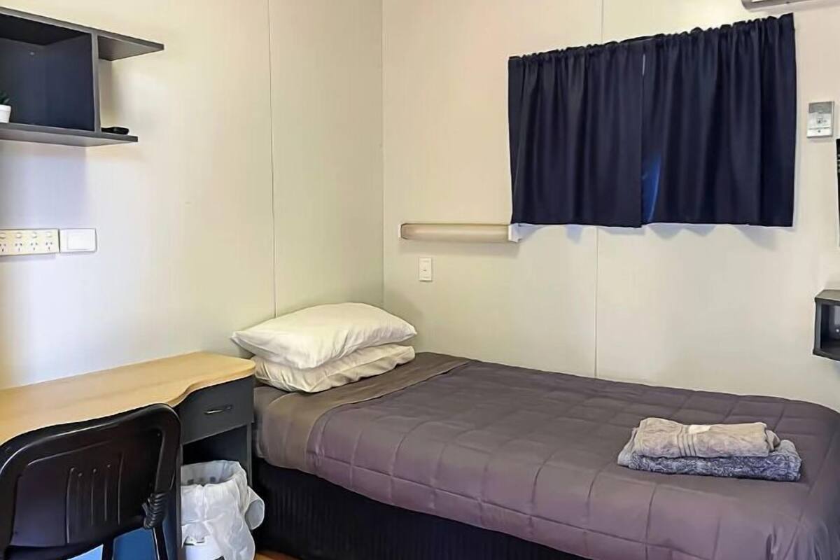 Una habitación pequeña con cama individual, escritorio, silla y ventana con cortinas.