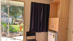 Una habitació petita amb un llit, una cadira, un armari de fusta i una finestra amb cortina.