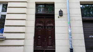 Fachada de edificio de diseño simétrico, con una entrada central con puertas dobles, flanqueada por ventanas con molduras decorativas.