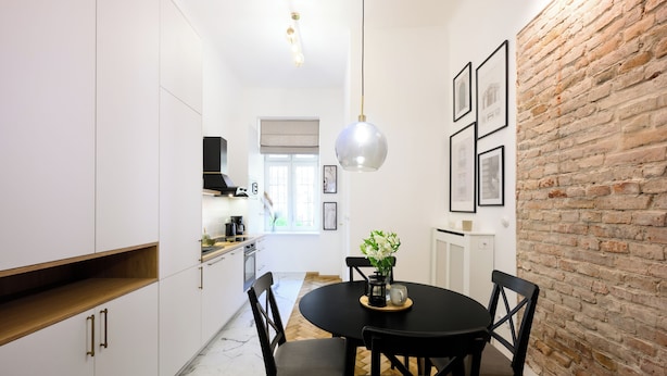 Una cocina moderna con armarios blancos, un comedor con mesa negra y una pared de ladrillo.