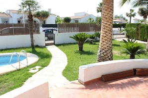 Une piscine avec une terrasse carrelée, un chemin pavé et un palmier.