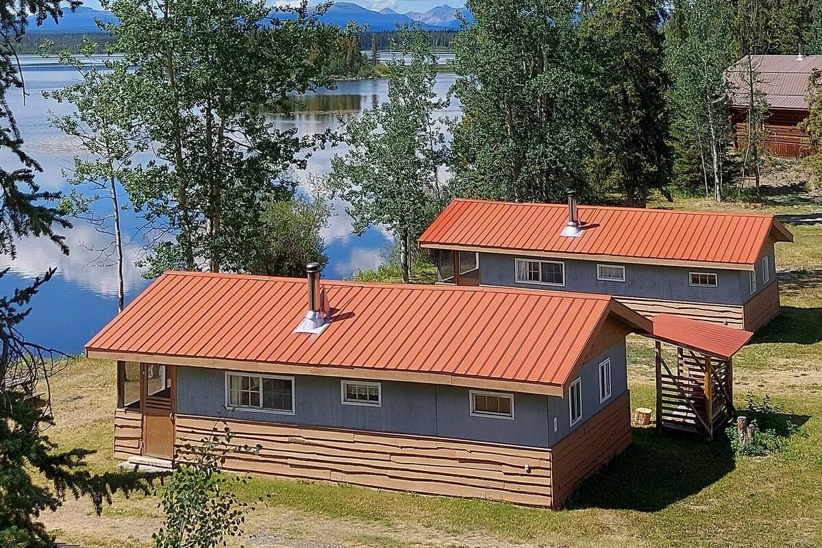 Two cabins with red roofs, wooden siding, and a view of a lake.
