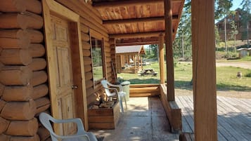 Una cabaña de troncos con un porche, bancos de madera y una mesa de picnic.