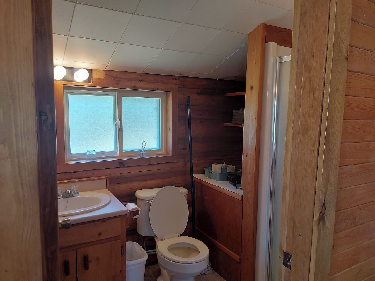 Ein kleines Badezimmer aus Holz mit Waschbecken, Toilette und Fenster.