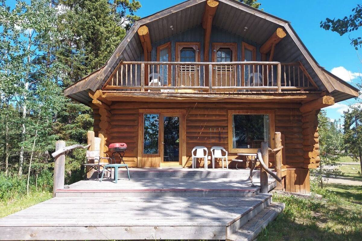 A log cabin with a balcony, a porch, and outdoor seating.