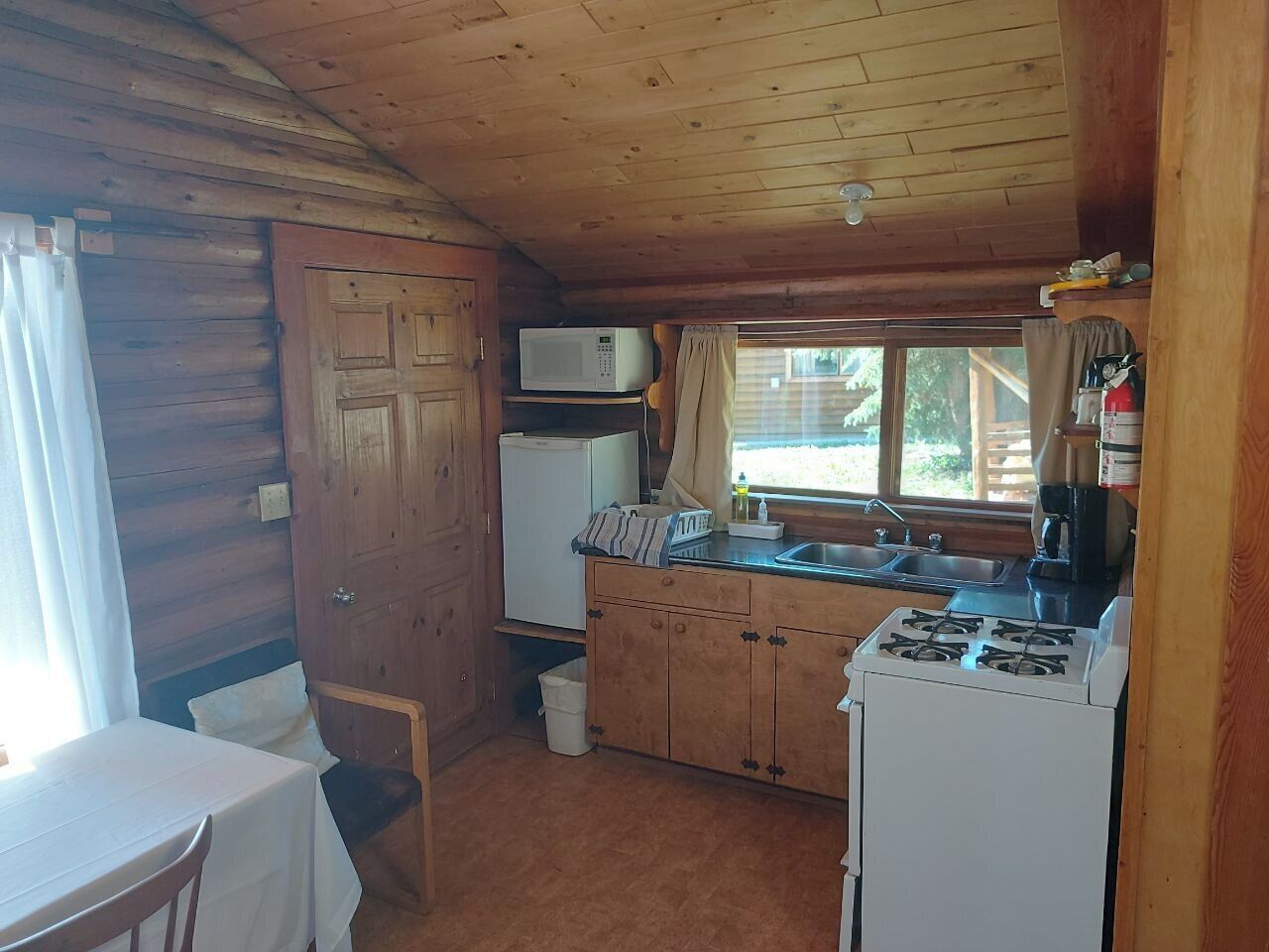 Pieni, käytännöllinen keittiö, jossa on puukalusteet, mikroaaltouuni, kaasuliesi ja pesuallas.