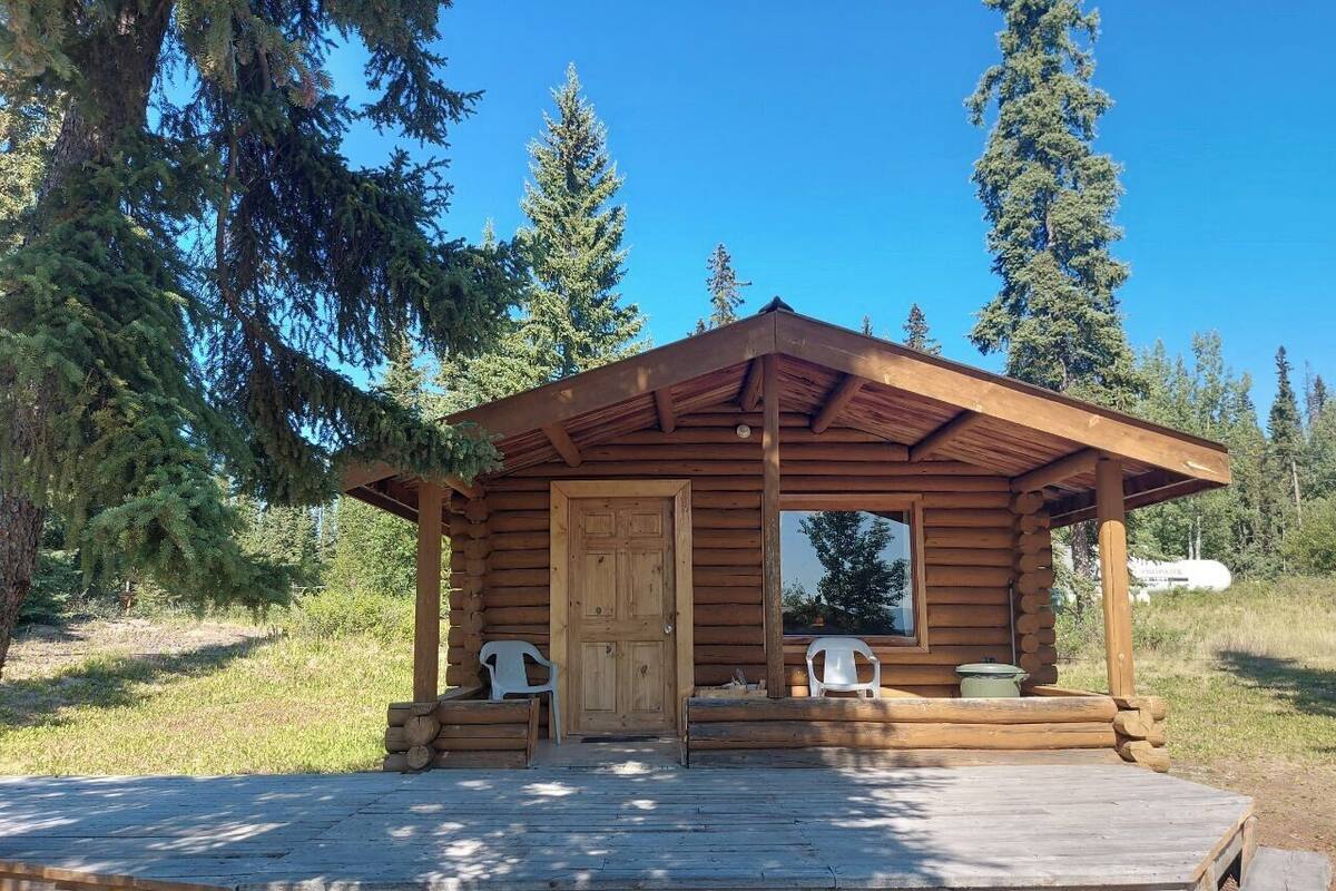 A wooden cabin with a porch, two chairs, and a door.