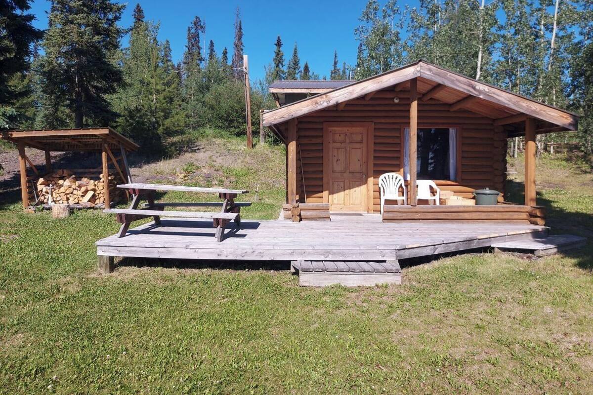 A wooden cabin with a porch, picnic table, and chairs.