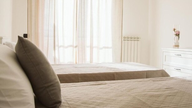 A bedroom with two beds, a white dresser, and a window with sheer curtains.