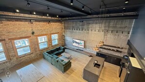 A spacious room with a green sofa, a coffee table, a TV mounted on the wall, and a kitchen area with a sink and countertop. - Pet Friendly Loft / Rooftop Hot Tub & Views (Fernie)