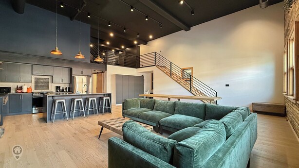 A modern kitchen with a central island, bar stools, and a staircase leading to an upper level. - Pet Friendly Loft / Rooftop Hot Tub & Views (Fernie)